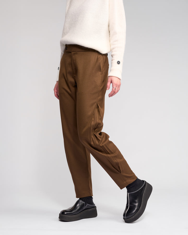 A person wears the Knewe Label Jude Pant in Cedar, paired with a white sweater and black platform shoes. Only their lower half is visible, highlighting the modern finish of these relaxed-leg, ankle-grazer pants against a plain light background.